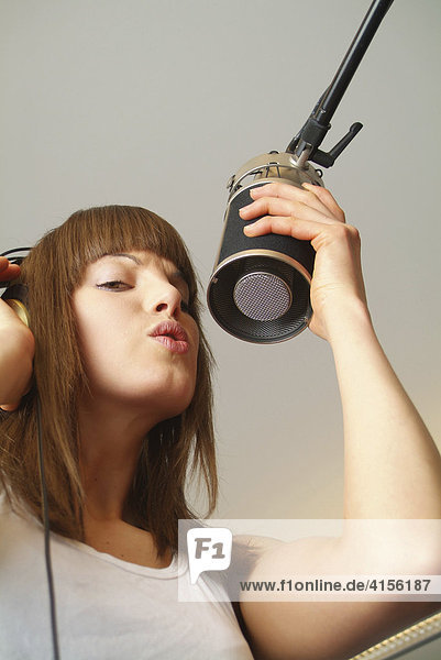 Junge Frau mit Kopfhörer singt am Mikrofon eines Tonstudios