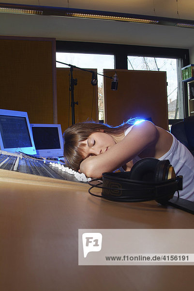 Junge Frau schläft erschöpft am Mischpult eines Tonstudios