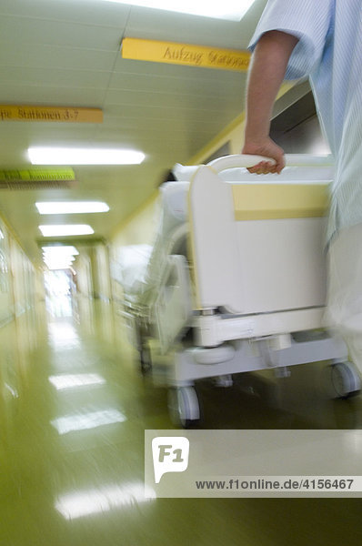 Pleger schiebt Krankenbett durch Flur
