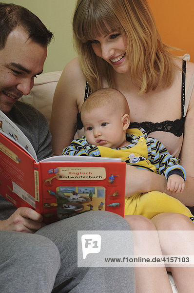 Vater  Mutter und Baby sehen sich Bildwörterbuch an