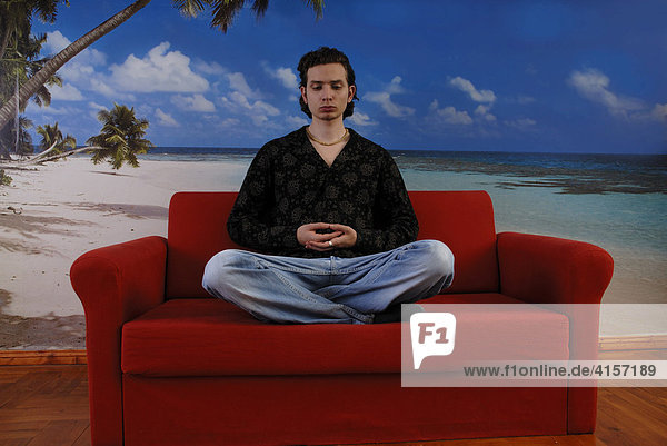 Mann meditiert auf einem roten Sofa vor einer Fototapete