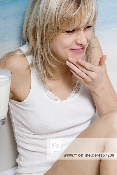 Blonde Frau in Unterwäsche frühstückt im Bett und trinkt ein Glas Milch und hat gekleckert