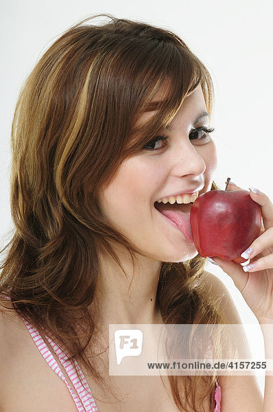 Hübsche junge braunhaarige Frau beißt in einen roten Apfel