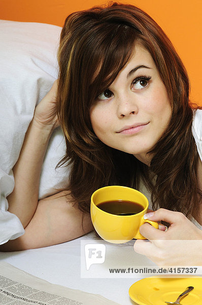 Young woman drinking coffee in bed and reading the newspaper