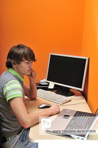 Junger Mann sitzt am Schreibtisch mit Computern und arbeitet