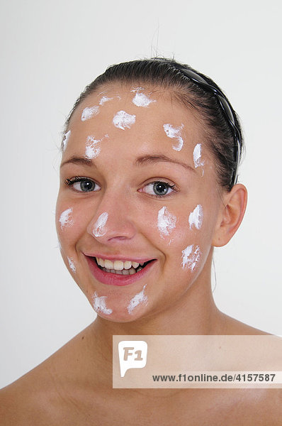 Junge  Frau hat Creme-Tupfer im Gesicht vor weißem Hintergrund