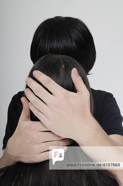 Hände eines Mannes umfassen Kopf einer jungen Frau  schwarze Haare  von hinten
