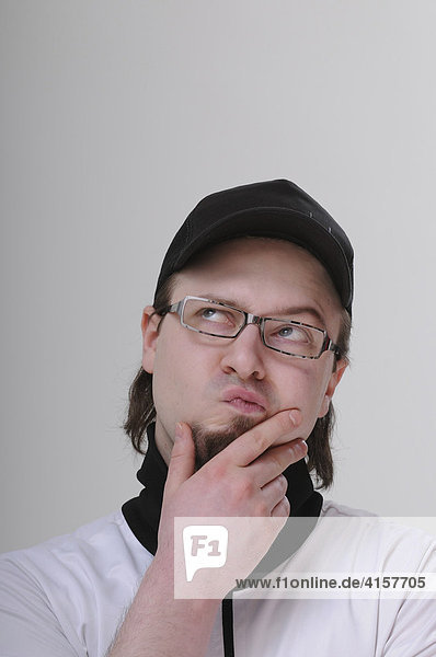 Young man with a goatee wearing glasses and a black baseball cap looking pensive