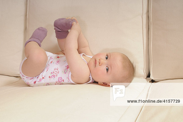Baby in Unterhemd  Body  7 Monate  auf Sofa  spielt mit Socken  Füßen  von der Seite