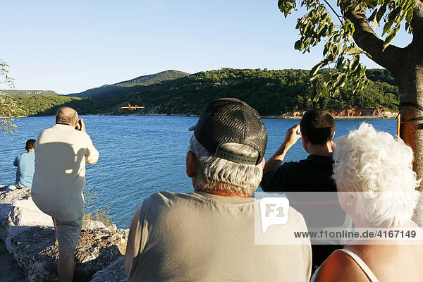 Touristen und Einheimische betrachten und fotografieren ein Feuerlöschflugzeug der französischen Feuerwehr  bzw. des Securité Civile  im Anflug auf den Lac de St. Croix  Provence  Frankreich.