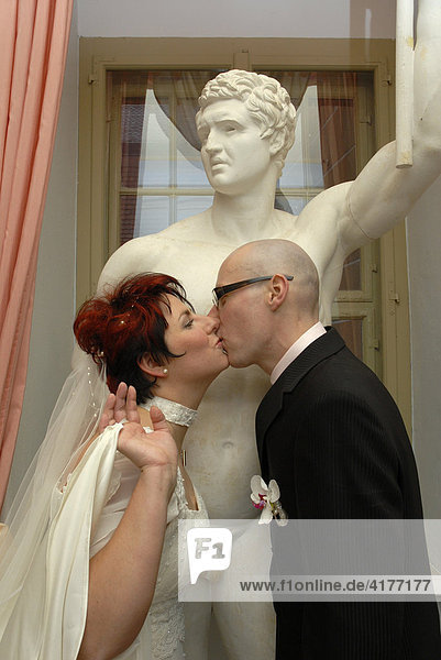 Hochzeitspaar küssend vor Statue