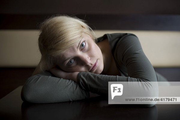 Blonde Frau liegt traurig mit dem Oberkörper auf einem Tisch in einer Bar