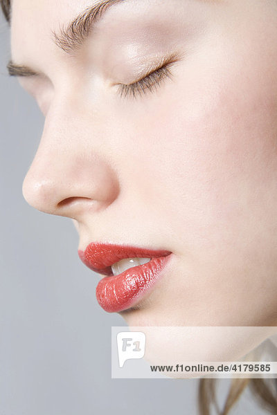 Nahaufnahme des Gesichts einer jungen Frau mit roten Lippen und geschlossenen Augen im Profil mund
