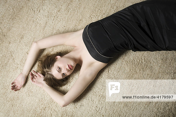 Junge Frau liegt mit schwarzem Kleid auf einem Teppich
