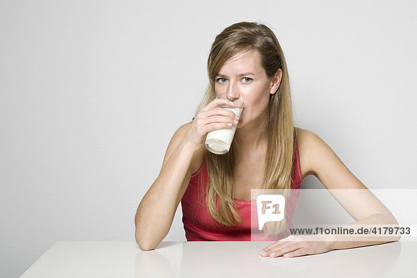 Young woman sitting at a table drinking a glass of milk