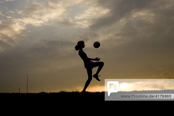 Silhouette einer jungen Frau beim Fußballspielen vor abendlichem Himmel