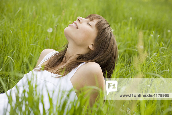 Young  dark-haired woman wearing a white dress  relaxed  lying in a meadow  enjoying the summer