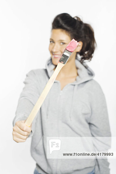 Young woman smiling into the camera holding in her hands a paintbrush dipped in pink paint