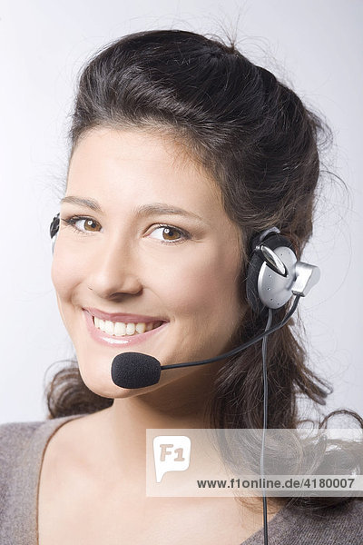 Junge dunkelhaarige Frau lacht beim Telefonieren mit Headset