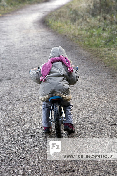 Young child biking down a asphalt path in wintertime