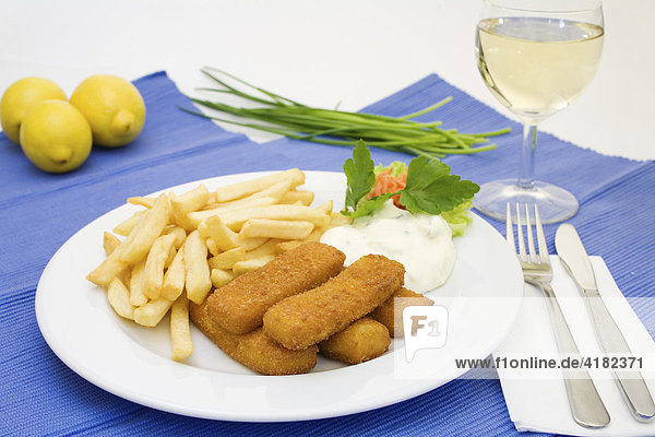 Fish sticks  tartar sauce and french fries served with a glass of white wine  lemons and chives