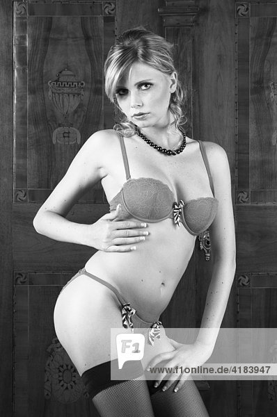 Junge Frau in erotischer Pose in einer Hotelsuite vor altem Kasten  schwarzweiß