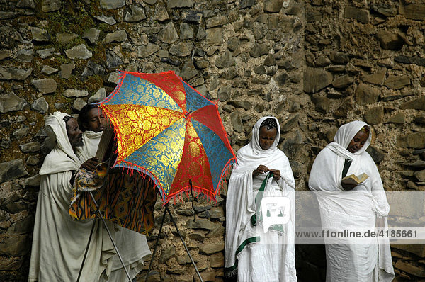 Christliche Gläubige in weißem Umhang und mit buntem Schirm an einer Mauer der Dreieinigkeitskirche Debre Berhan Selassie  Gondar  Äthiopien  Afrika