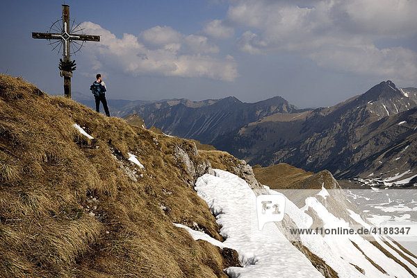 Mountain climber at the summit  standing beside summit cross  Allgaeu Alps  Hinterstein  Tirol  Austria  Europe