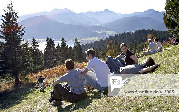 Tegernsee  GER  30. Oct. 2005 - People sitting on a meadow in front of the Neureuthaus on the footpath between Schliersee and Tegernsee in Bavaria. In the background the Tegernsee is visible.