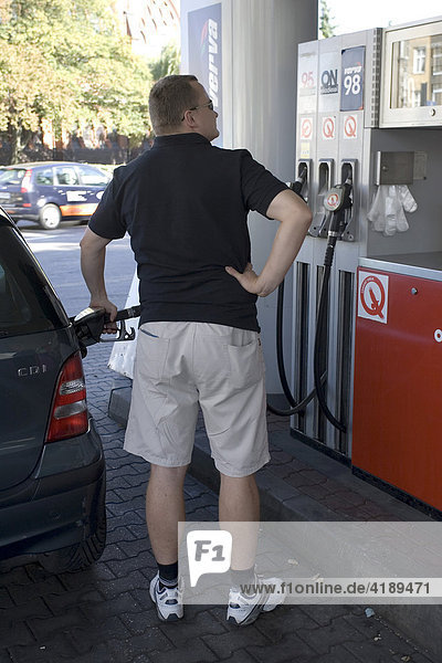 Mann betankt sein Auto und schaut dabei auf die Benzinuhr