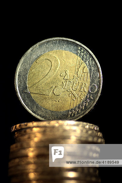 Eine 2 Euromünze stehend auf einem Stapel Euromünzen mit schwarzem Hintergrund