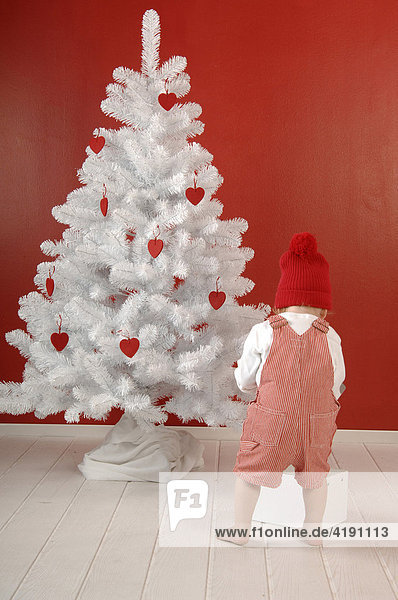 Kind mit Geschenk vor Weihnachtsbaum