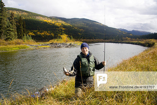 Fisherman and his catch standing on the bank of Big Salmon River  Yukon Territory  Canada