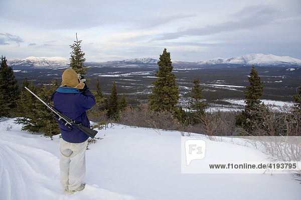 Hunter with a rifle looking for game though binoculars  Yukon Territory  Canada  North America