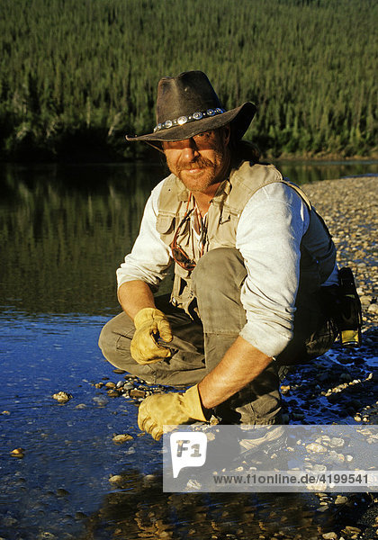 Man crouching at river's edge  Brooks Range  Alaska