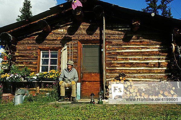 Elderly man sitting in front of his log home  Brooks Range  Alaska  USA