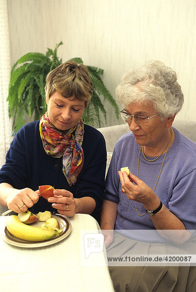 Frau schneidet Seniorin Obst in kleine Stücke