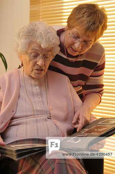 Elderly woman and her daughter looking through an old photo album filled with family portraits