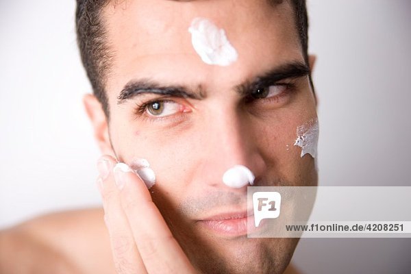 Young man applying facial cream.