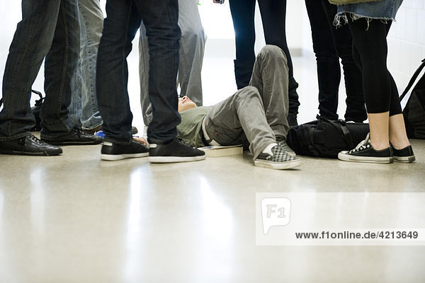 Bullies surrounding and threatening teenage boy lying on floor