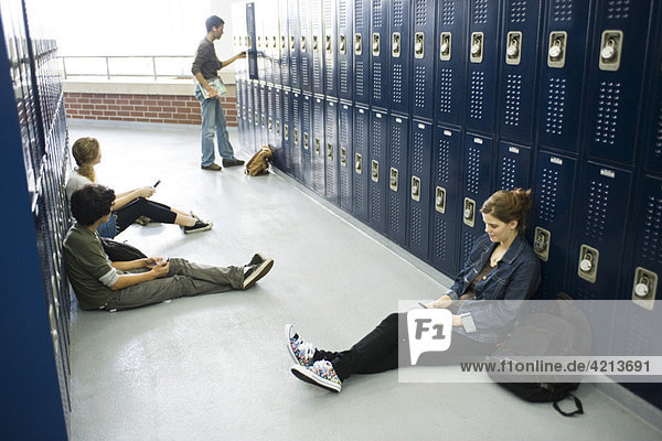 Gymnasiasten sitzen auf dem Boden durch Schließfächer mit Hilfe von Handys
