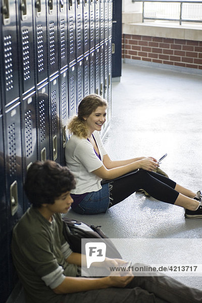 Gymnasiast sitzend auf dem Boden bei einem Schließfach mit Handy