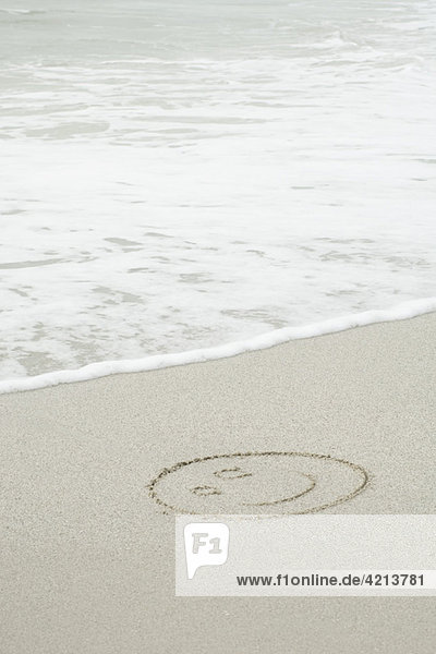 Smiley Gesicht in Sand am Strand gezeichnet