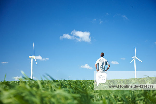 Mann im Feld schaut auf Windkraftanlagen