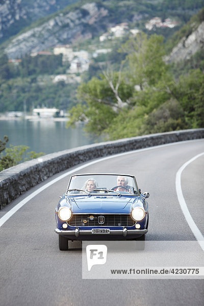 Seniorenpaar fährt mit Cabrio auf Küstenstraße  Italien  Navene