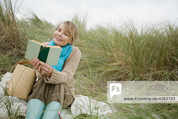 Frau beim Lesen eines Buches auf einer Düne