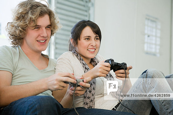 Teenage couple playing with games consoles