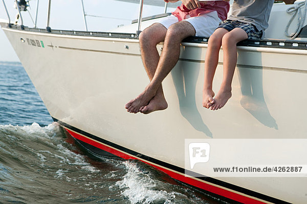 Vater und Sohn auf der Yacht sitzend  Beine baumelnd