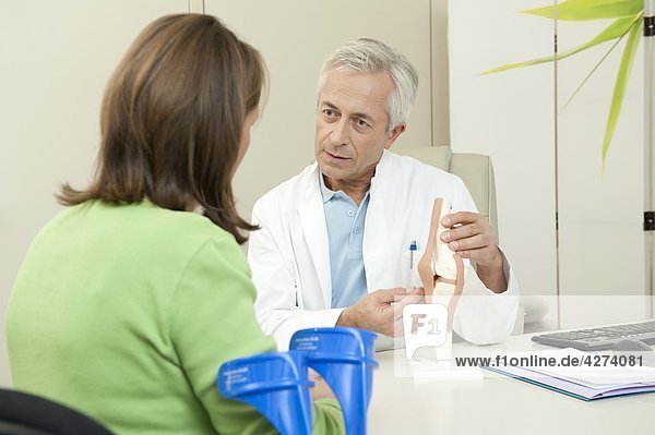 Arzt zeigt einer Patientin ein künstliches Kniegelenk