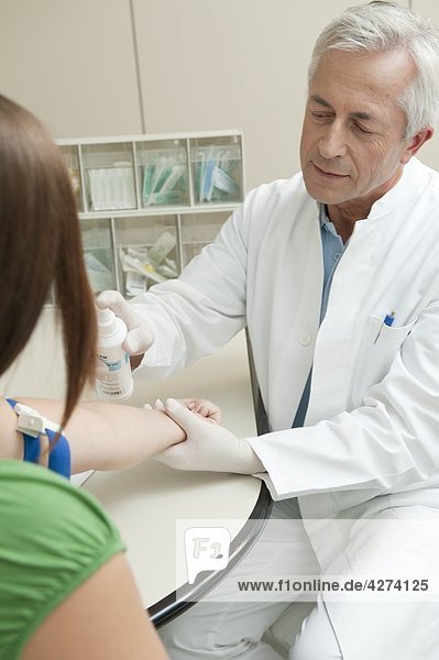 Arzt desinfiziert den Arm einer Patientin